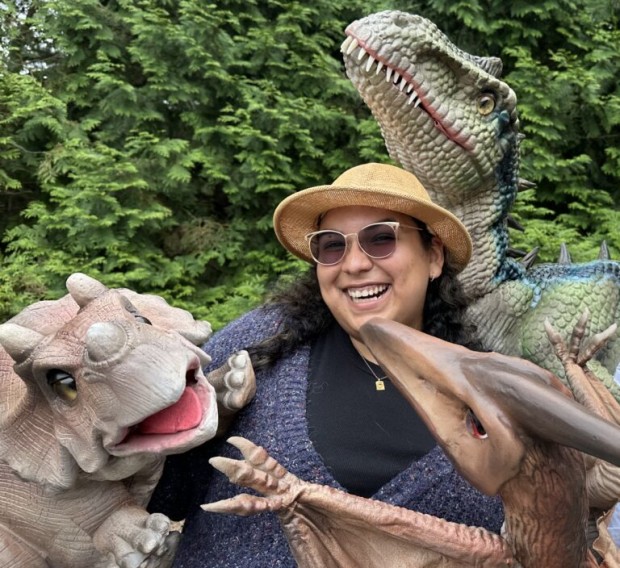 A smiling woman is surrounded by lifelike dinosaur puppets